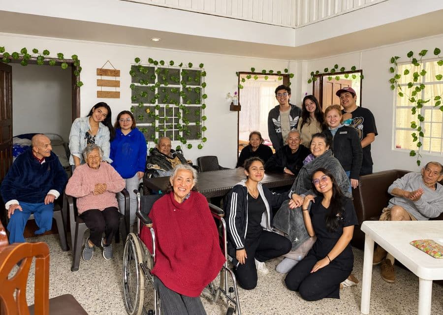 Personas mayores del programa reunidas con jóvenes voluntarios en la sala de la casa